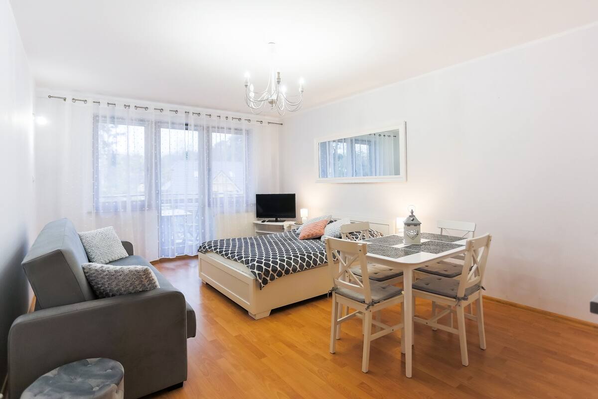 Ein modernes Schlafzimmer mit Bett, Sofa, Esstisch mit Stühlen, Fernseher und einer Kristallleuchter.
