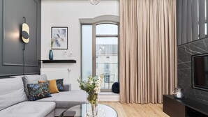 Un salon moderne avec un canapé gris, une table basse en verre, un téléviseur et une grande fenêtre avec des rideaux.