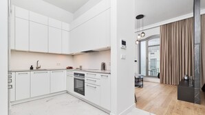 Une cuisine moderne avec des meubles blancs, un four encastré et un coin repas doté d’un plancher en bois et donnant sur l’extérieur grâce à une porte vitrée.