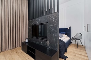 A modern bedroom with a TV mounted on a marble wall, a bed with a blue headboard, and a black chair.
