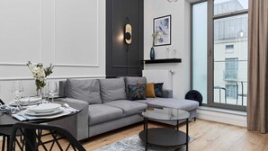 Un salon moderne avec un canapé gris, une table basse ronde et un coin repas où la table est déjà mise.