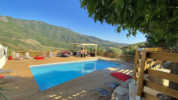 Eine Holzterrasse mit Schwimmbecken, Liegestühlen und einer Steinmauer.