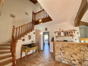 Un intérieur spacieux avec un escalier en bois, un comptoir en pierre et un coin repas comprenant des chaises et une table.