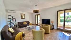 Ein Wohnzimmer mit einer Couch, Sesseln, einem Couchtisch, einem Fernseher und einem Bücherregal.