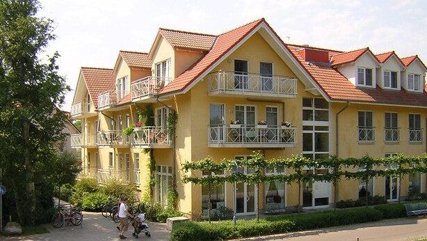 A yellow multi-story building with balconies, a paved entrance, and a clear sky.