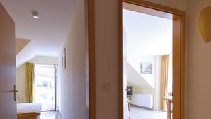 A hotel room with a bed, a desk, and a chair. There is a window with curtains and a door leading to another room.