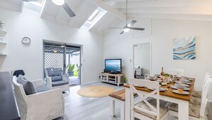Un vaste espace de vie comprenant une table à manger dressée pour le repas, un téléviseur et un ventilateur de plafond.
