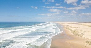 Een strand met golven, zand en een heldere lucht.