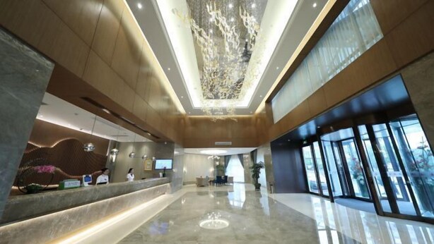 A modern hotel lobby with a reception desk, seating area, and large windows.