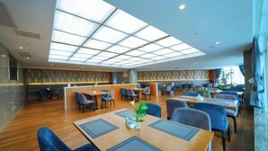 A modern hotel lobby with a central reception desk, multiple seating areas, and a large skylight.