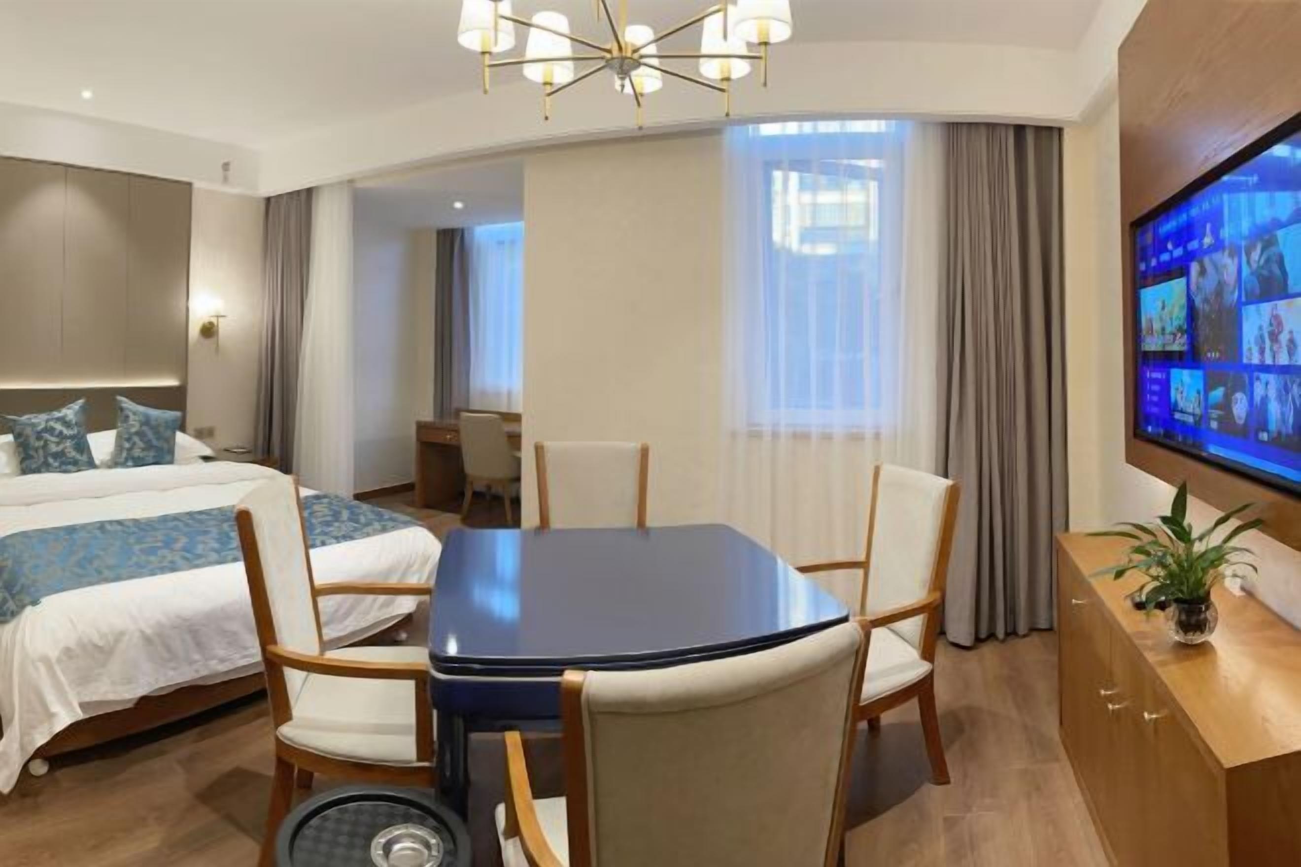 Una habitación de hotel con cama, una mesa de comedor con sillas, televisor y mostrador de recepción.