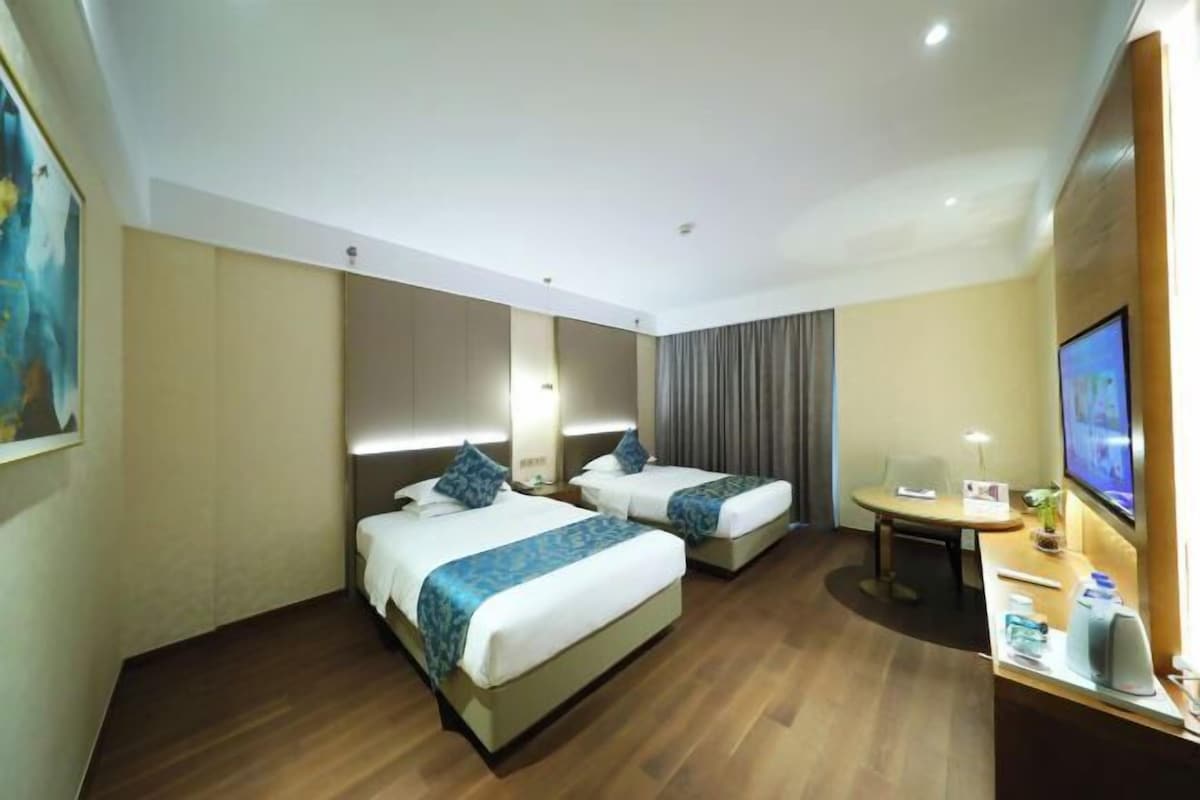 A hotel room with two beds, a desk, a TV, and a painting on the wall.