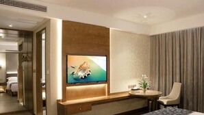 A hotel room with a bed, a TV mounted on the wall, a small table with a chair, and a potted plant.