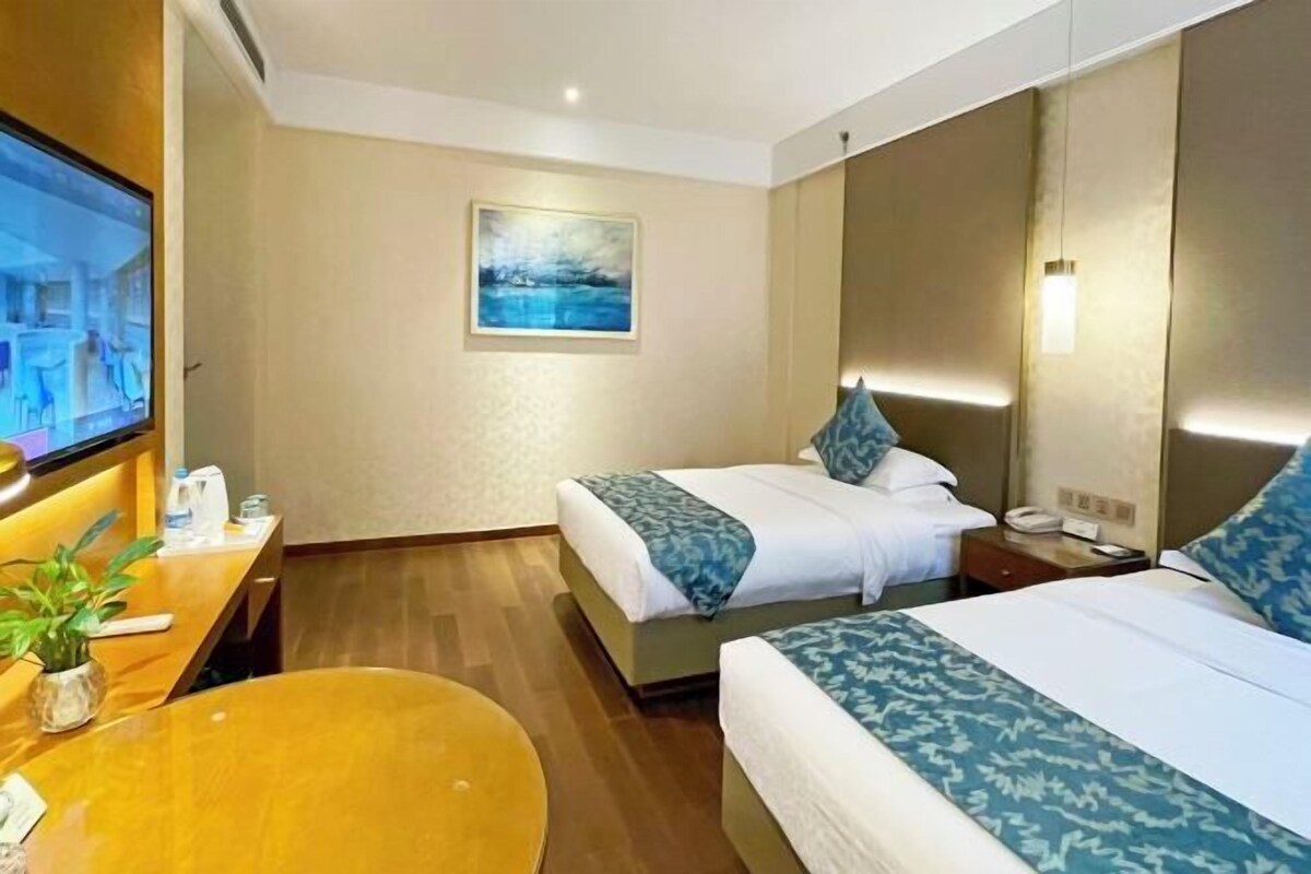A hotel room with two beds, a TV, a desk with a plant, and a painting on the wall.