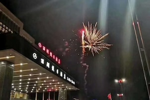 Entrada de hotel de diseño moderno, con un letrero llamativo con caracteres iluminados y una exhibición de fuegos artificiales visible al fondo.