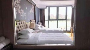 Une chambre d’hôtel avec un grand lit, un lit plus petit, un coin salon avec une chaise et une table, et une vue sur l’extérieur grâce à une grande fenêtre.