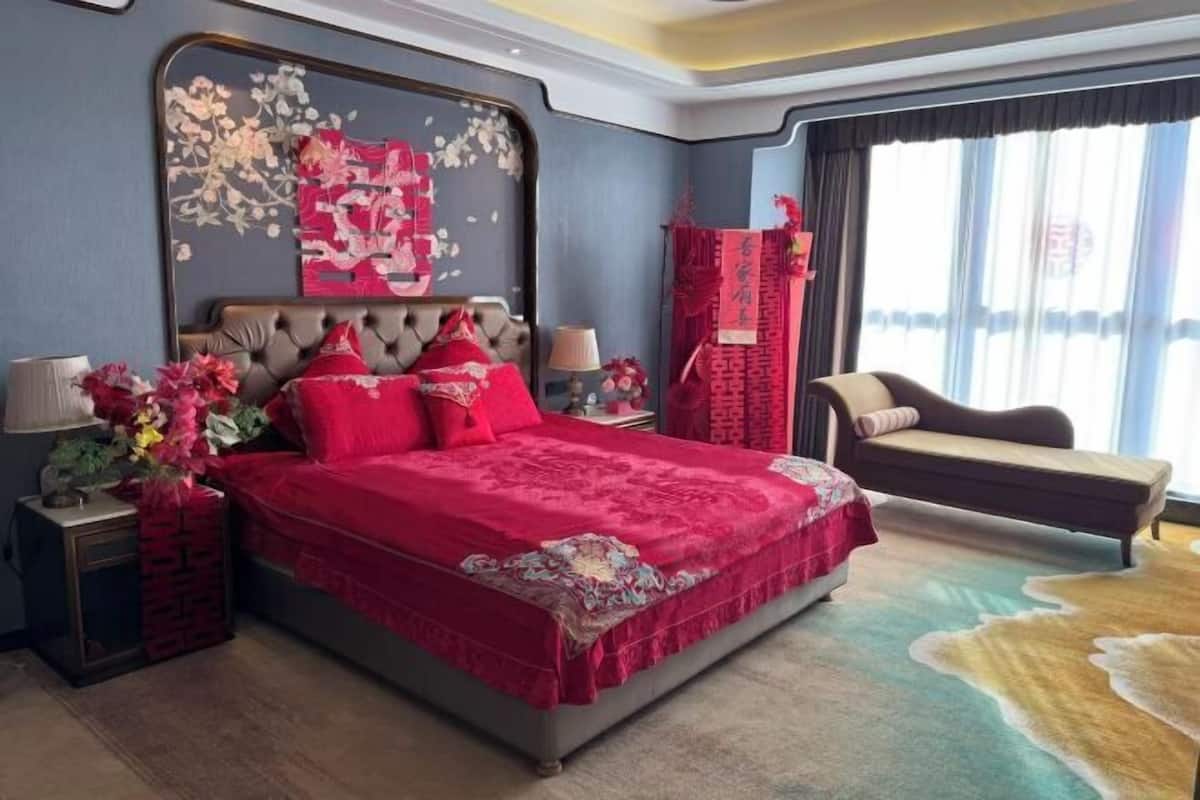 A bedroom with a large bed, a nightstand, a chair, and a decorative wall piece.
