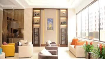 A modern hotel lobby with seating areas, a reception desk, and a large window offering a view of the cityscape.