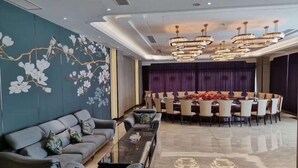 Un espace de repas moderne avec une table ronde et des chaises, un canapé avec des coussins et un mur décoratif orné de motifs floraux.