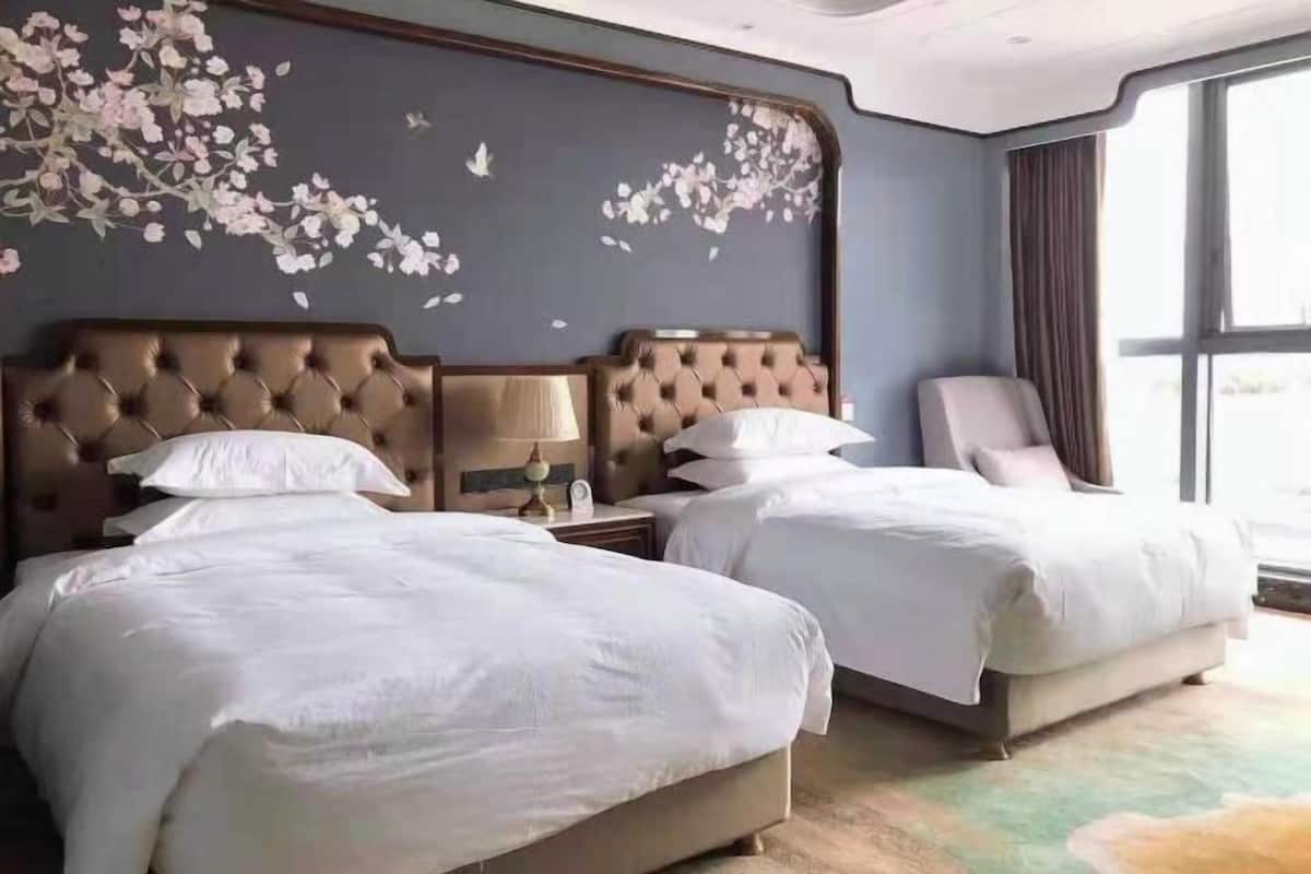 A hotel room with two beds, a large window, and a wall with floral artwork.