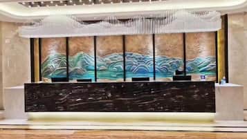 A reception desk with a modern design, a large wall painting, and a decorative ceiling feature.