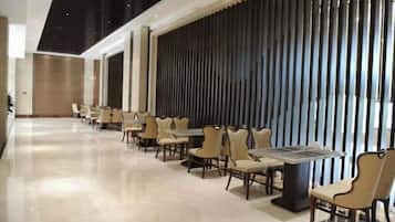 A hotel lobby with a long row of tables and chairs, a modern ceiling design, and a decorative wall with vertical elements.