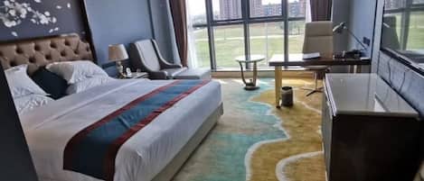 A hotel room with a large bed, a desk, a chair, and a view of the city through large windows.