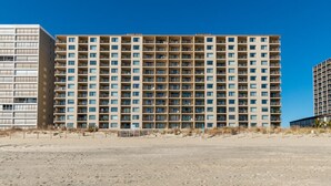 A multi-story hotel with a uniform facade, balconies, and a sandy foreground. - New Listing! Beautiful ocean front views, just steps to the beach. (Ocean City)