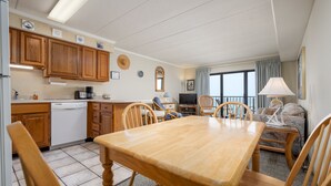 A compact kitchen with wooden cabinets, a dishwasher, and a dining area with a wooden table and chairs. - New Listing! Beautiful ocean front views, just steps to the beach. (Ocean City)