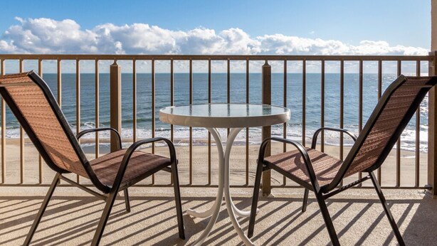 A balcony with two chairs and a table, overlooking the ocean with a clear sky. - New Listing! Beautiful ocean front views, just steps to the beach. (Ocean City)