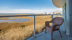 En balkon med en fletstol, der udover et kystlandskab med vådområder og bygninger i det fjerne.
