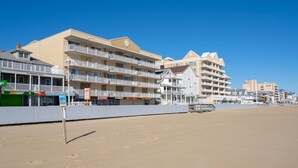 A beachfront hotel with multiple balconies, a sandy beach in the foreground, and various storefronts including a Subway. - New Listing!  Large luxury condo on the boardwalk with pool! (Ocean City)