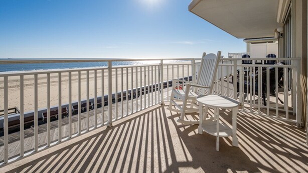 A balcony with a view of the beach, white chairs, and a sunshade. - New Listing!  Large luxury condo on the boardwalk with pool! (Ocean City)