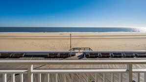 A beach view from a wooden deck with lounge chairs and a railing. - New Listing!  Large luxury condo on the boardwalk with pool! (Ocean City)
