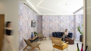 A modern living room with patterned wallpaper, a blue sofa, wicker chairs, and a coffee table. - Casual Raizes Porto Hotel by Casual Hoteles (Porto)