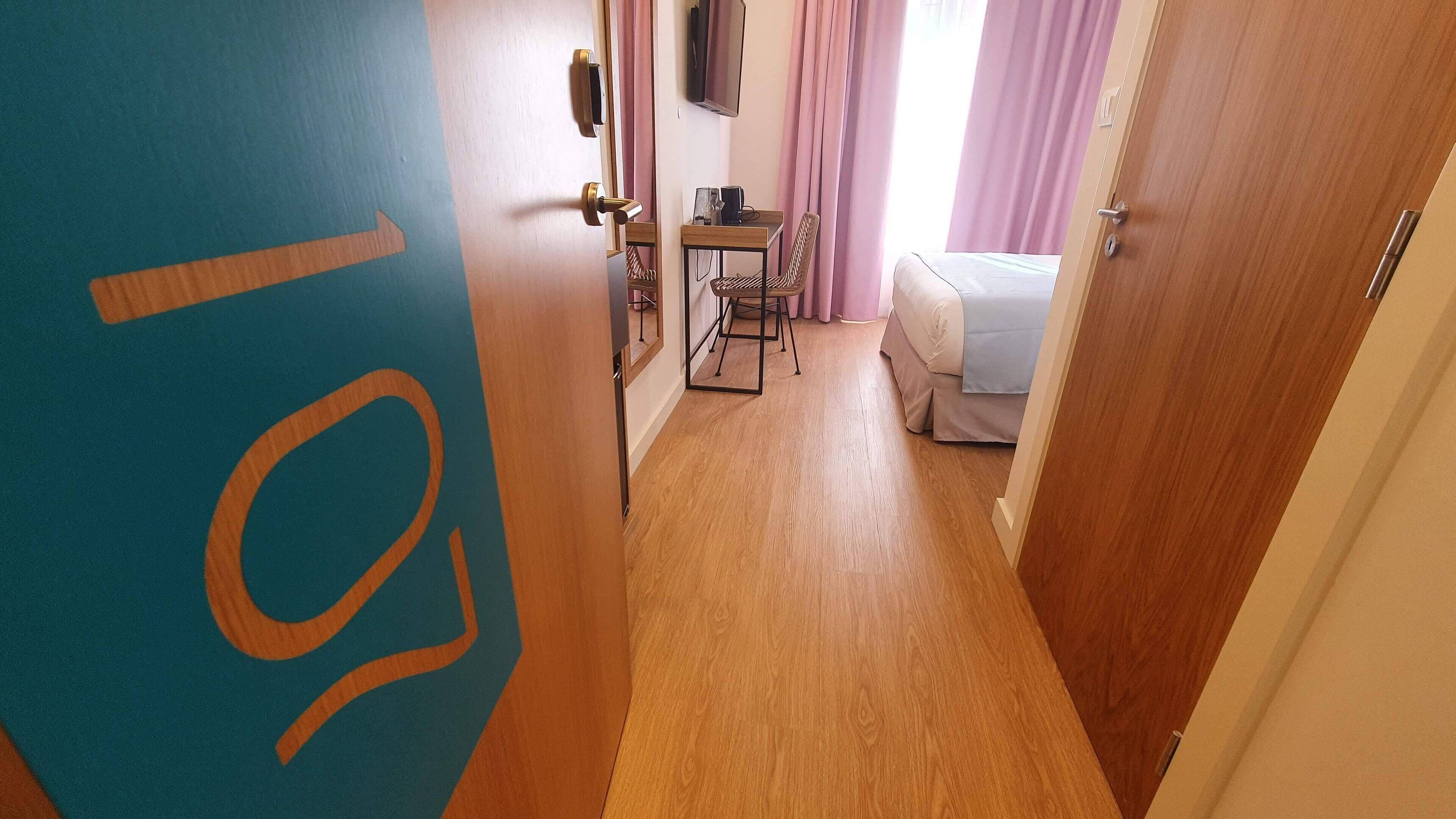 A hotel room with a bed, a desk with a chair, a television, and a door with a number.