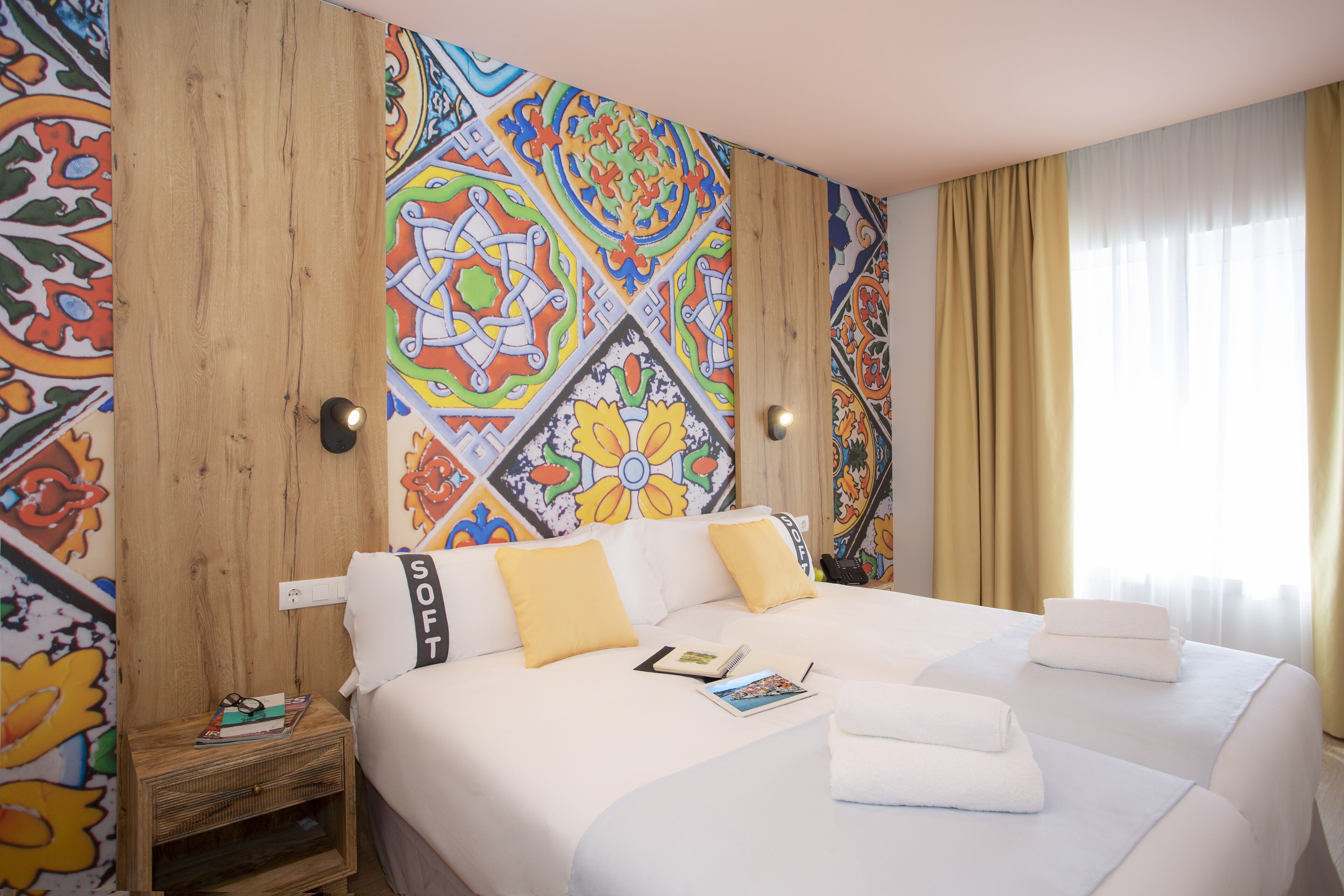 A hotel room with a large bed, two pillows, a nightstand, and a colorful wall mural.