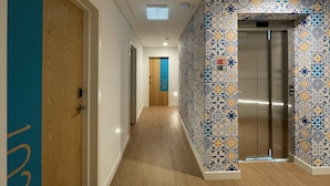A hallway with a wooden door, a blue and white patterned wall, and an elevator. - Casual Raizes Porto Hotel by Casual Hoteles (Porto)