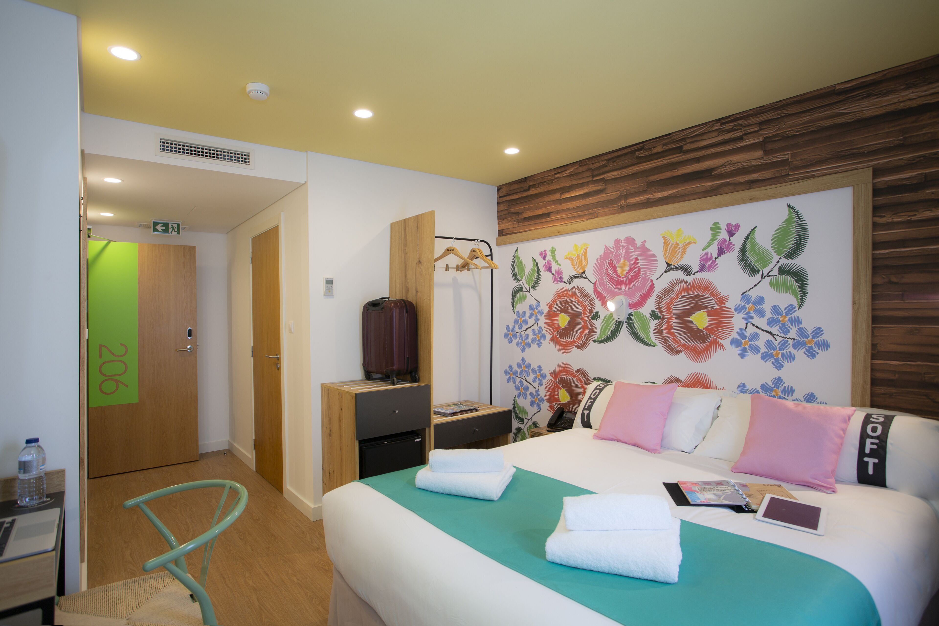 Una habitación de hotel con cama, escritorio, silla y una pared decorada con un mural floral.
