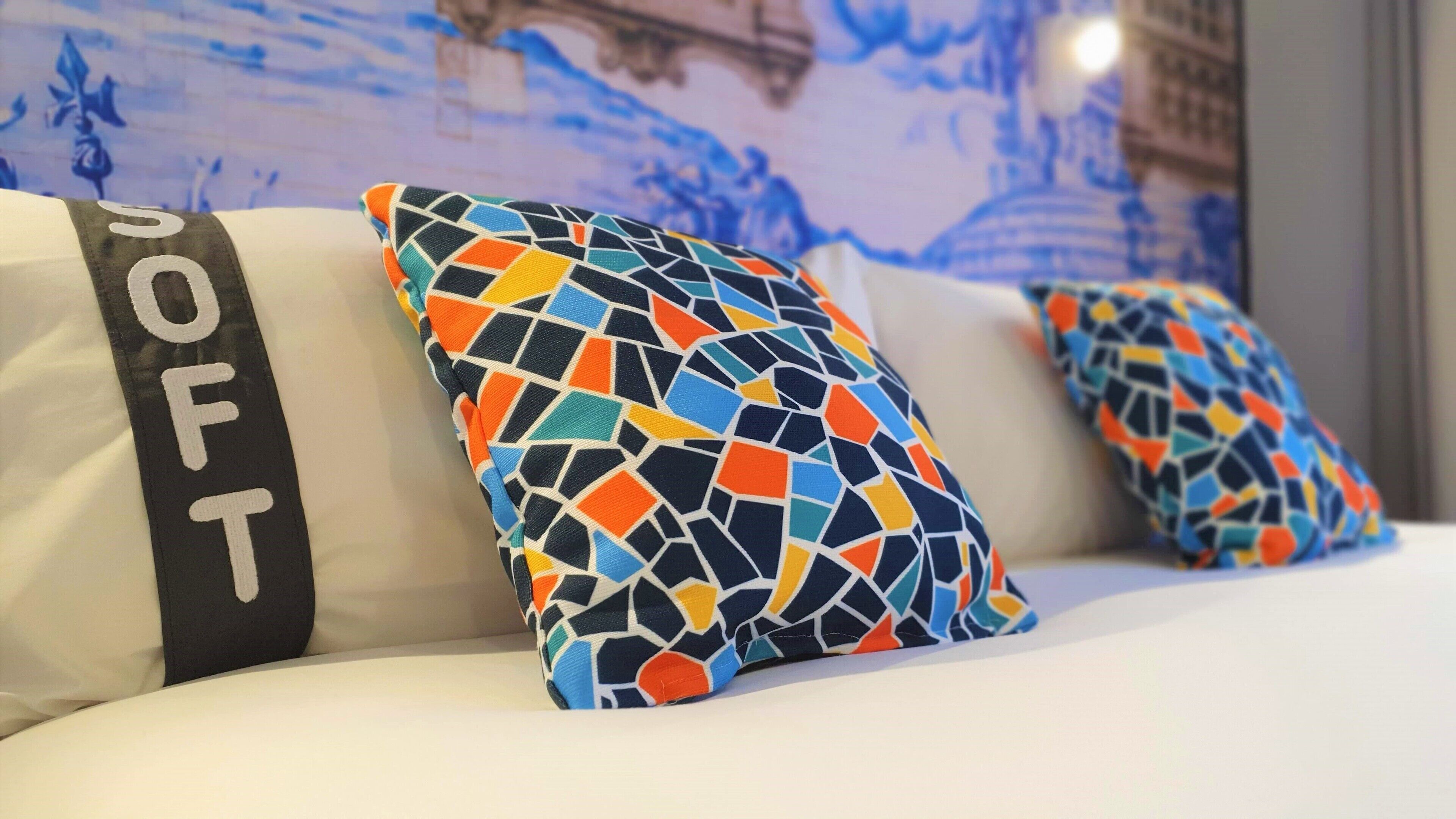 A bed with two pillows, one with a geometric pattern and the other with the word 'SOFT' on it.