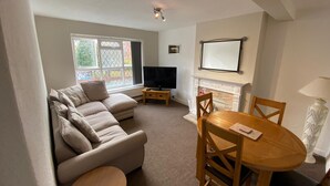 A living room with a sofa, TV, fireplace, and dining table. - Lovely 2-bed Apartment in Solihull (Solihull)