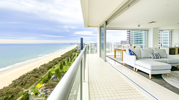 A balcony with a view of the beach and ocean, a sofa, and a dining area.