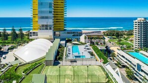 A modern hotel with a large swimming pool, a tennis court, and a view of the ocean.