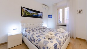 A bedroom with a bed, a nightstand, a window with curtains, and a wall-mounted air conditioner. - Designer apartment (Rapallo)