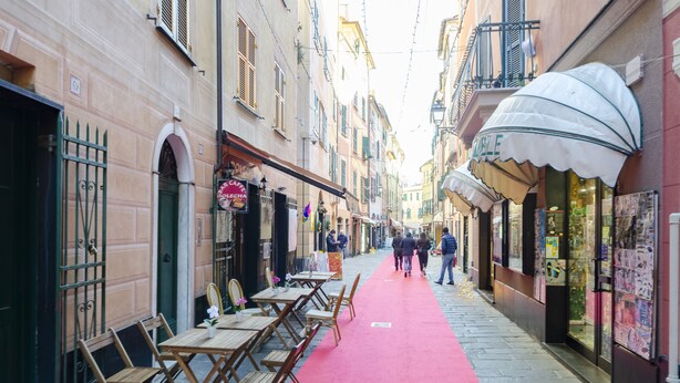 A narrow street with a red carpet, wooden tables, and chairs set up for outdoor dining. - Designer apartment (Rapallo)