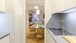 A modern kitchen with a stainless steel sink, a dining area with a round table and wicker chairs, and a pendant light fixture. - Designer apartment (Rapallo)