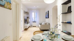 A modern living room with a sofa, a dining table set with plates and glasses, and a decorative vase with flowers. - Designer apartment (Rapallo)