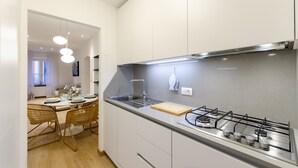 A modern kitchen with white cabinets, a gas stove, and a dining area with wicker chairs and a wooden table. - Designer apartment (Rapallo)