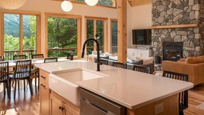 A spacious kitchen with a large island, wooden cabinetry, and a stone fireplace. - Luxury Chalet | Hot Tub | Minutes to Sunday River (Newry)