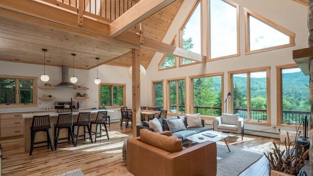 A spacious living area with a high ceiling, large windows, and a cozy seating arrangement. - Luxury Chalet | Hot Tub | Minutes to Sunday River (Newry)
